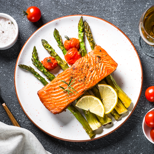 Baked salmon fish fillet with asparagus and tomato with glass wine on black stone table